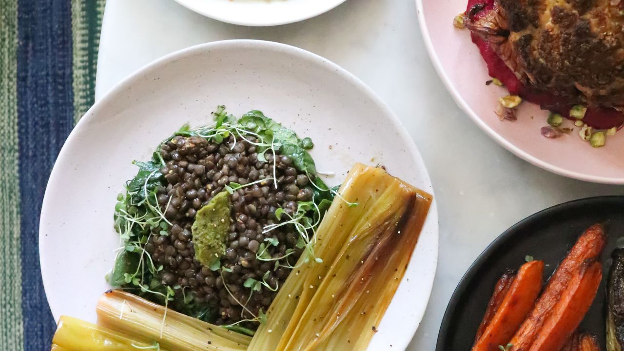 Overhead view of healthy plates with green lentils, fresh greens, roasted leeks and carrots on a light table