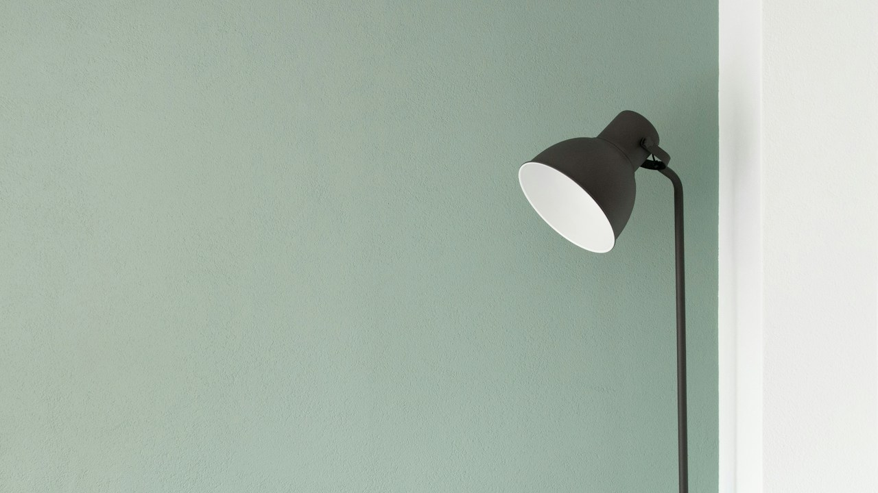 Minimal black floor lamp casting soft light against a sage green wall for quiet evenings