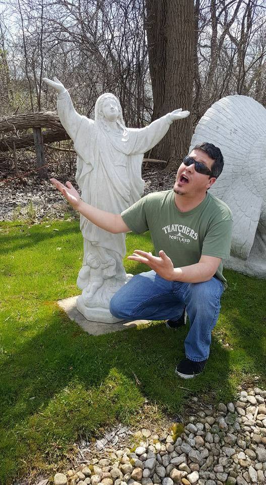 Brent crouching in front of an angel statue making silly faces.