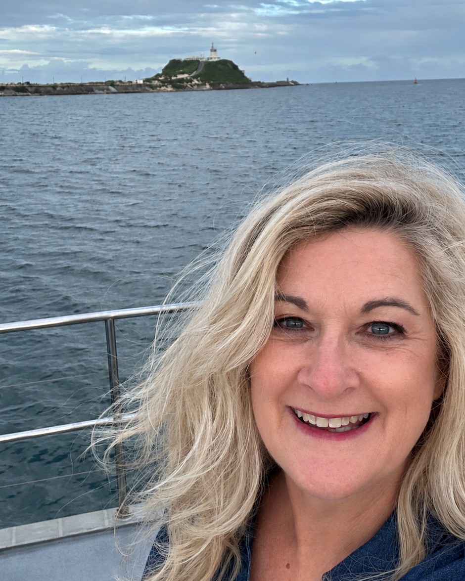 Liz Murray on Newcastle Harbour with the wind in her hair and the lighthouse behind her