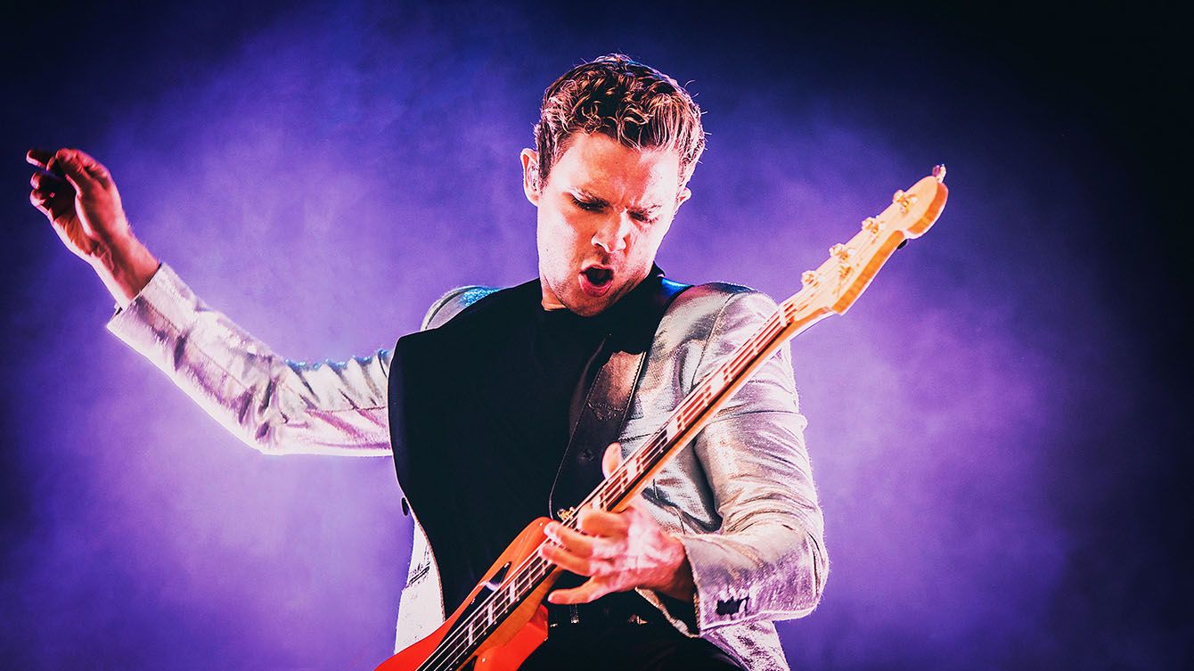 Royal Blood performing live, singer playing a red guitar under purple stage lights