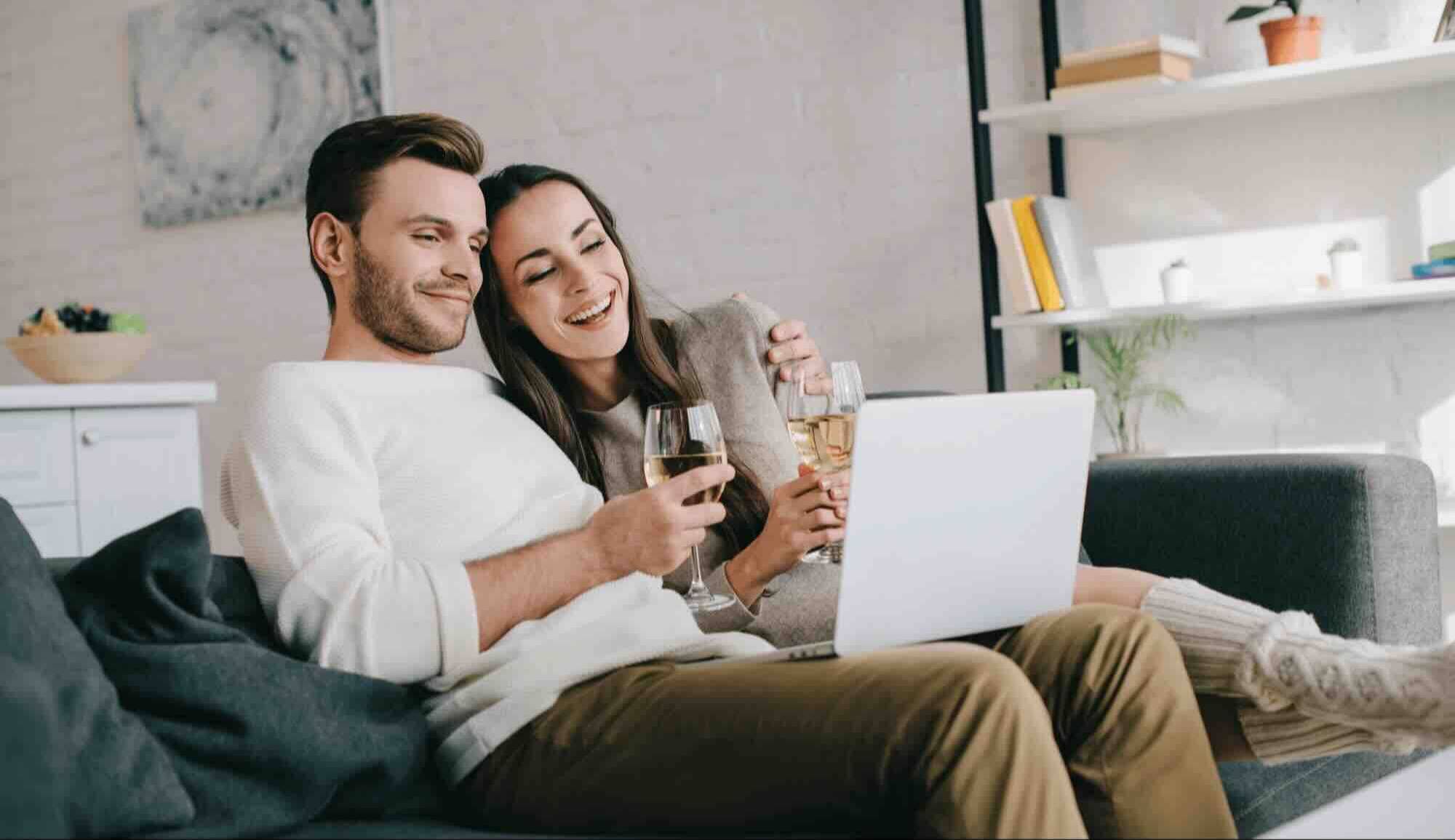 Stel volgt samen met een glas wijn een online wijncursus op de bank