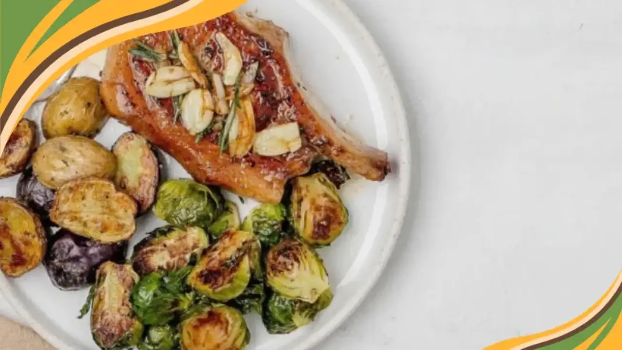 Plate of juicy pork chop with roasted Brussels sprouts and potatoes on a white background.