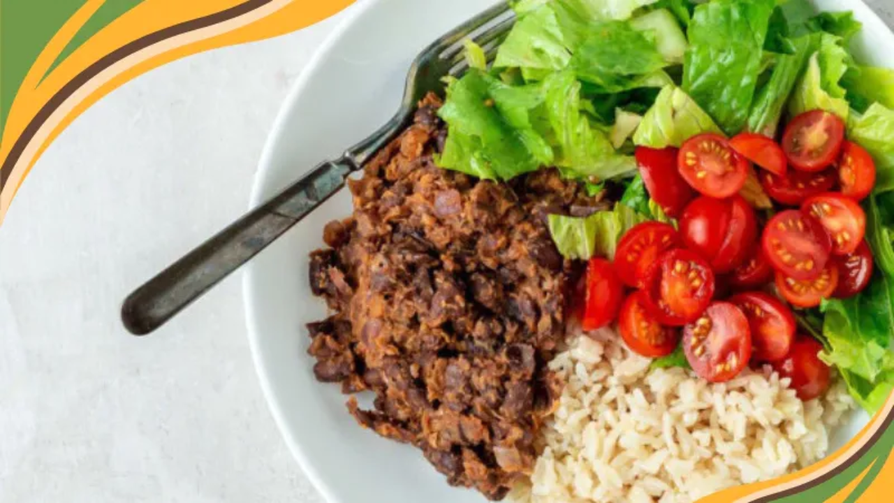 Healthy vegan plate with black beans, brown rice, fresh romaine lettuce, and cherry tomatoes on a white dish.