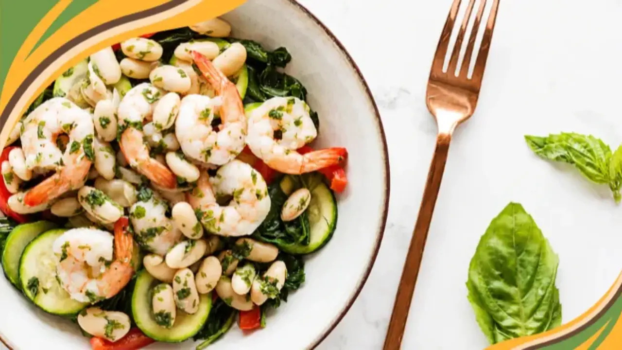 Healthy shrimp and white bean salad with zucchini, red bell peppers, and spinach in a white bowl.