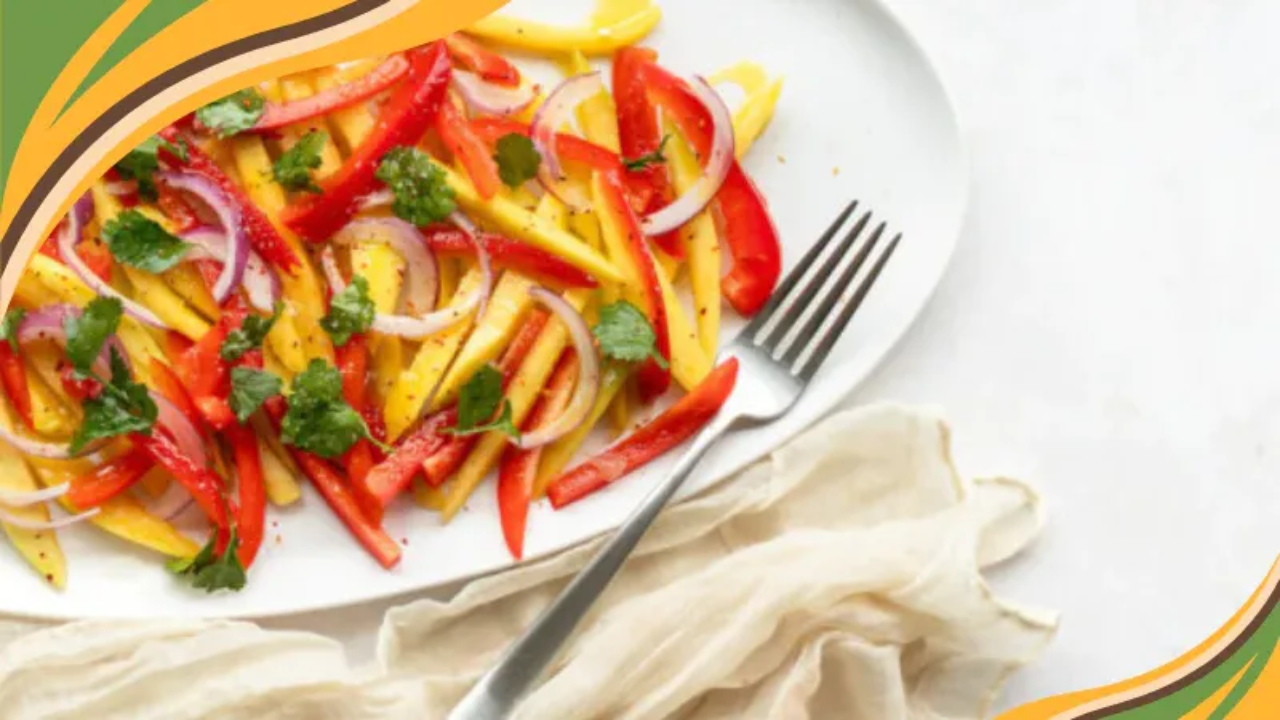 Colorful mango salad with red bell pepper, red onion, and fresh cilantro on a white plate with a fork.