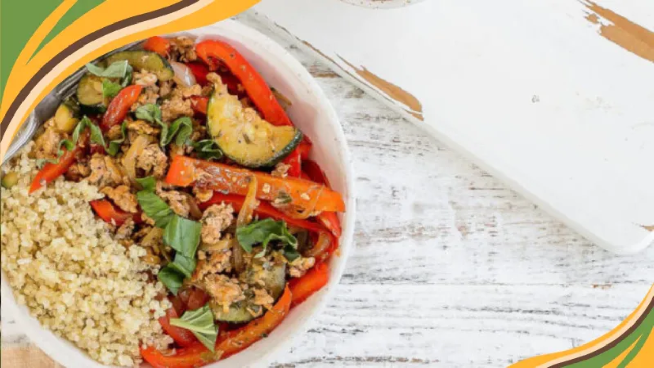 Colorful quinoa bowl with sautéed vegetables, ground meat, and fresh herbs on a rustic white wooden table.