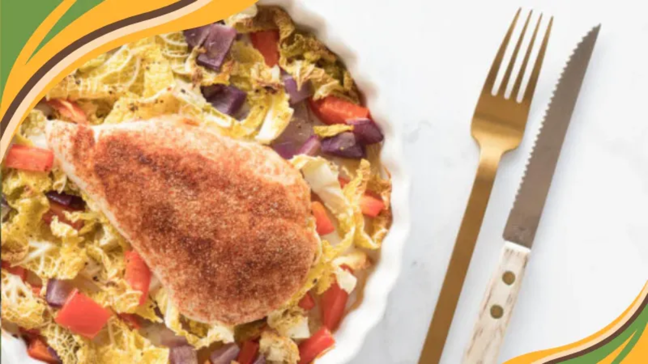 Baked chicken breast on a bed of roasted cabbage, red peppers, and purple onions in a white dish.