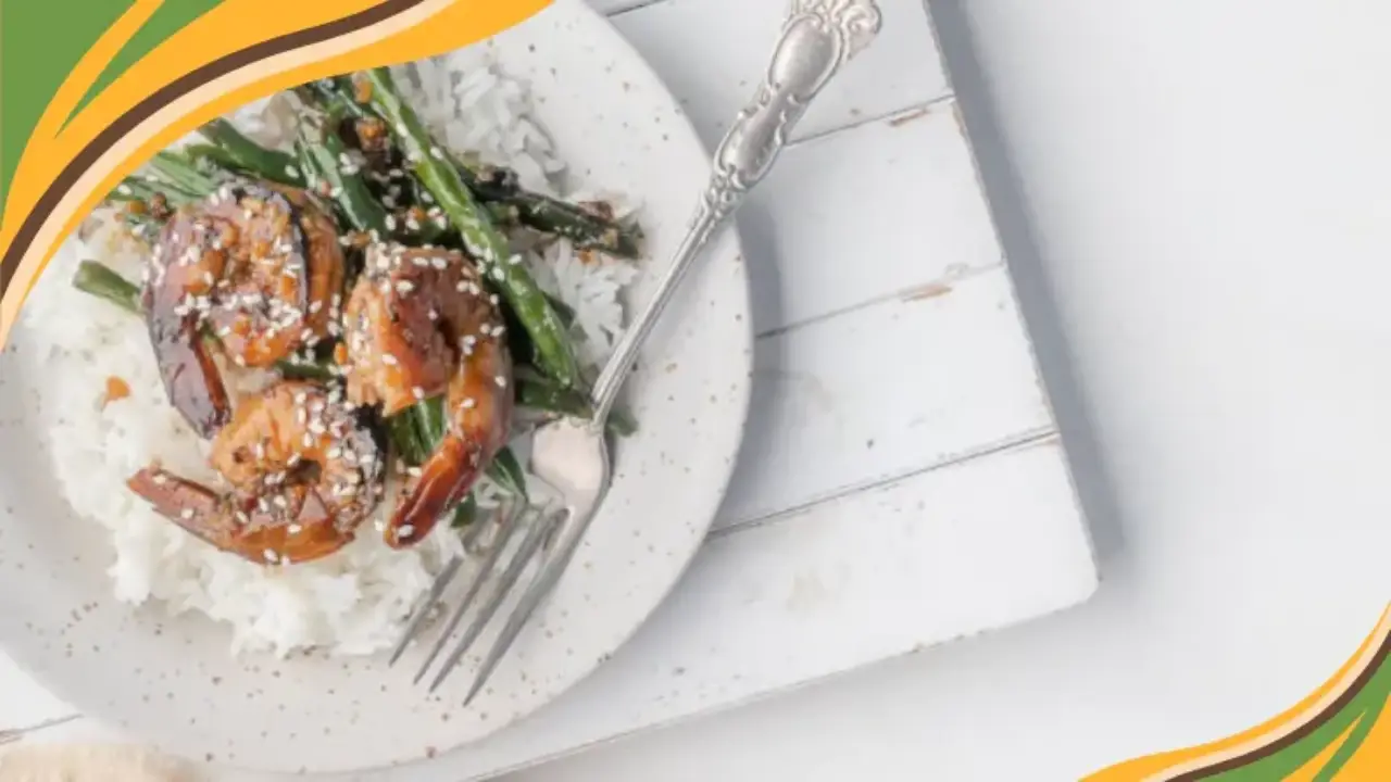 Teriyaki shrimp and green beans served over white rice, topped with sesame seeds on a rustic white plate.