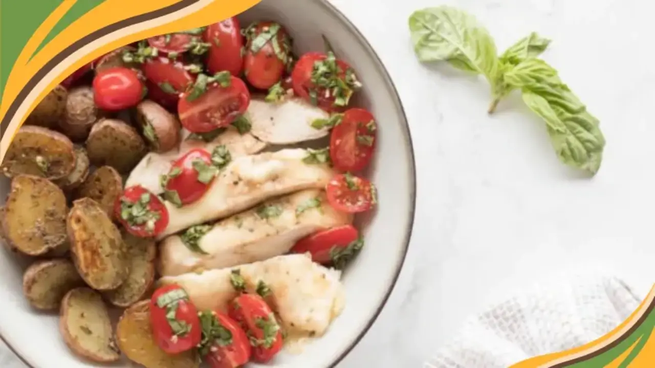 Plate with sliced chicken breast, roasted baby potatoes, and cherry tomatoes topped with fresh herbs.