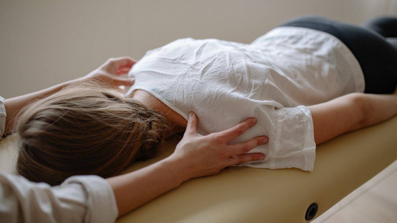 Woman clothed on massage table receiving gently bodywork and shoulder massage.