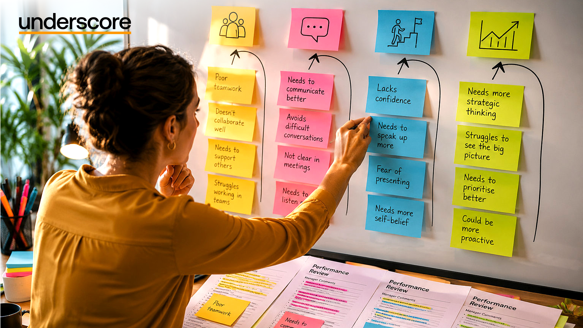 Professional reviewing performance appraisal feedback using colour-coded sticky notes grouped into development themes including teamwork, communication, confidence and strategic thinking, with performance review documents spread across a desk.