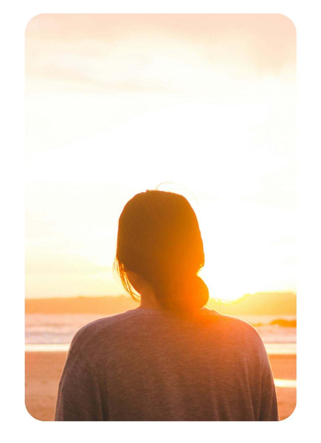 Woman standing at the beach at sunset, reflecting on her wellbeing and mental health journey