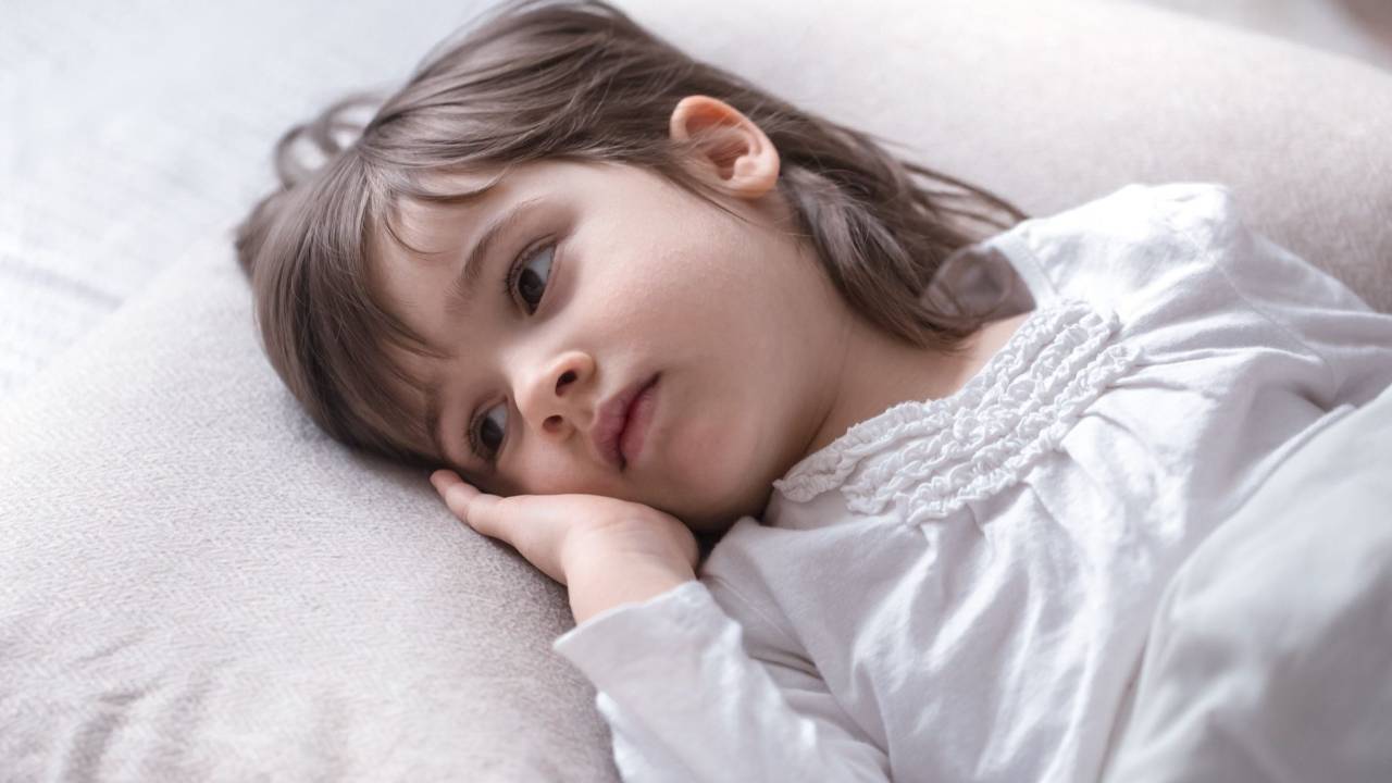 A young child resting her head on a pillow, awake and looking tired