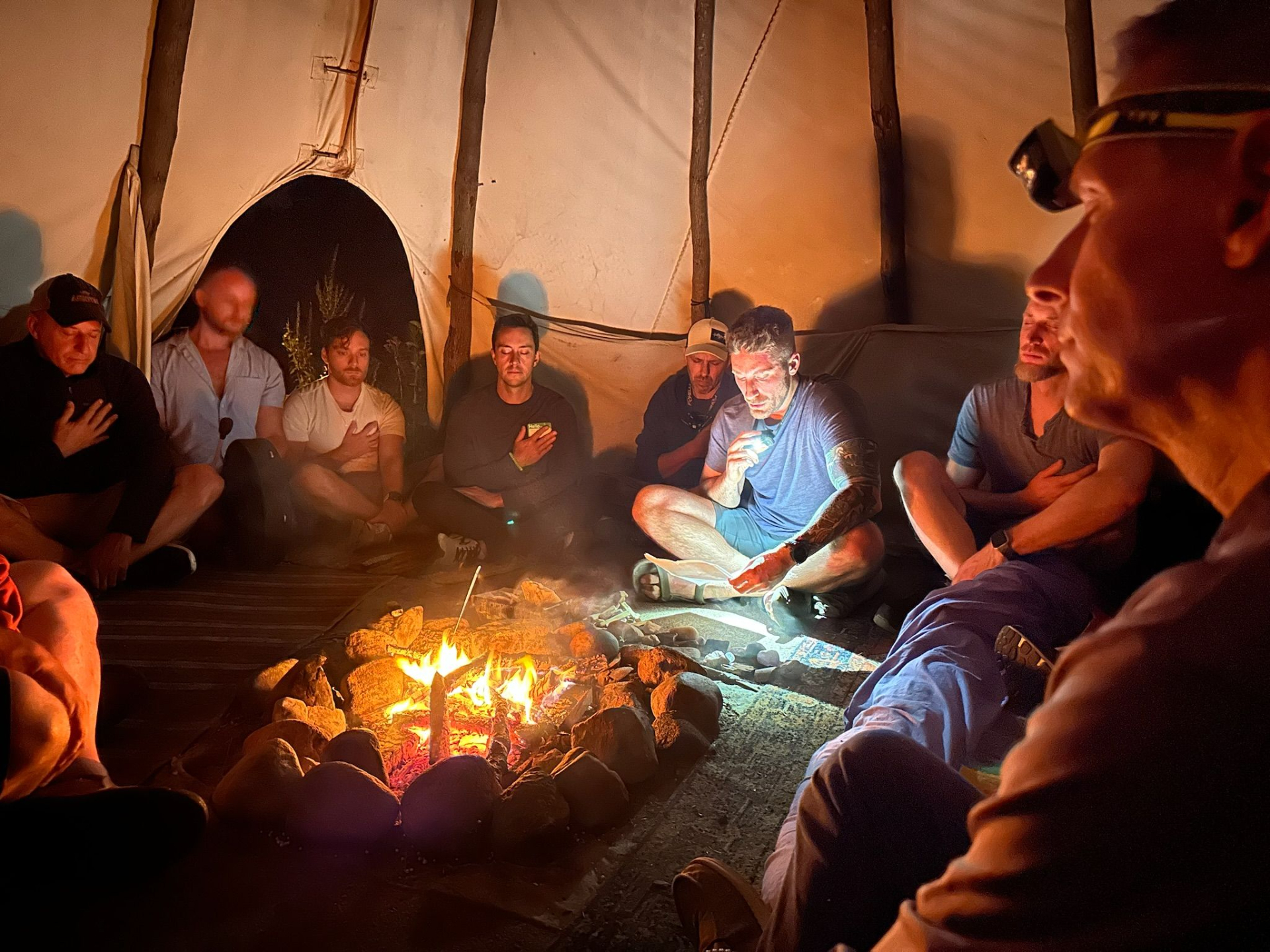 Men sitting in a circle around a fire inside the tipi during an evening council ceremony at the Annual Men's Retreat at Lynx Run, Michigan