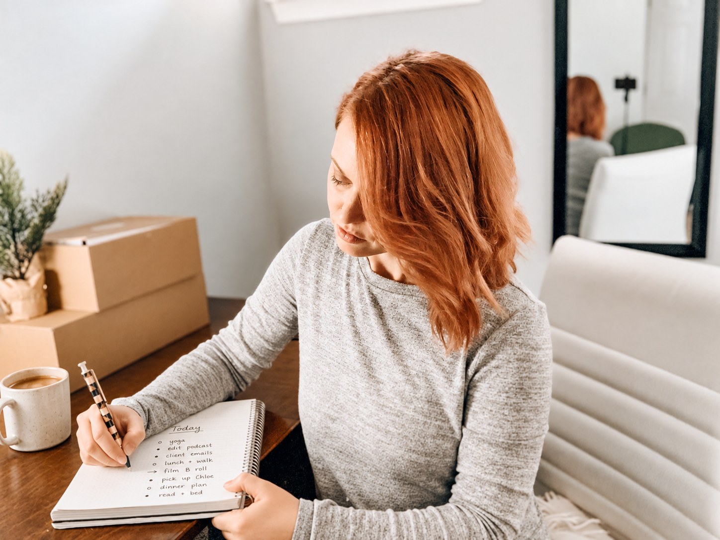 Woman writing a daily log in her bullet journal at her desk with a cup of coffee