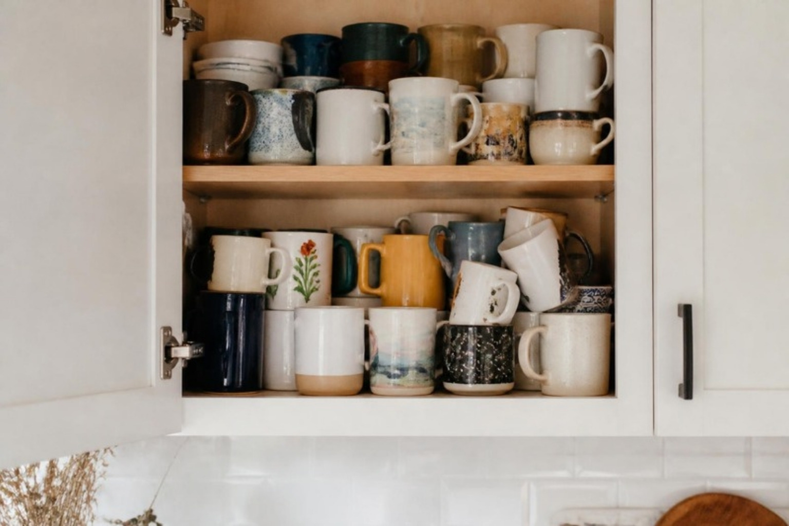 A kitchen cabinet crammed with mismatched coffee mugs