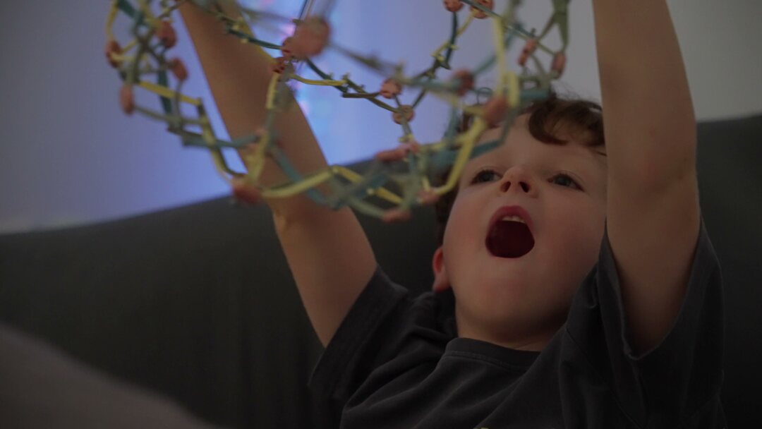 A young child holding an expanding breathing ball in front of a bubble tube