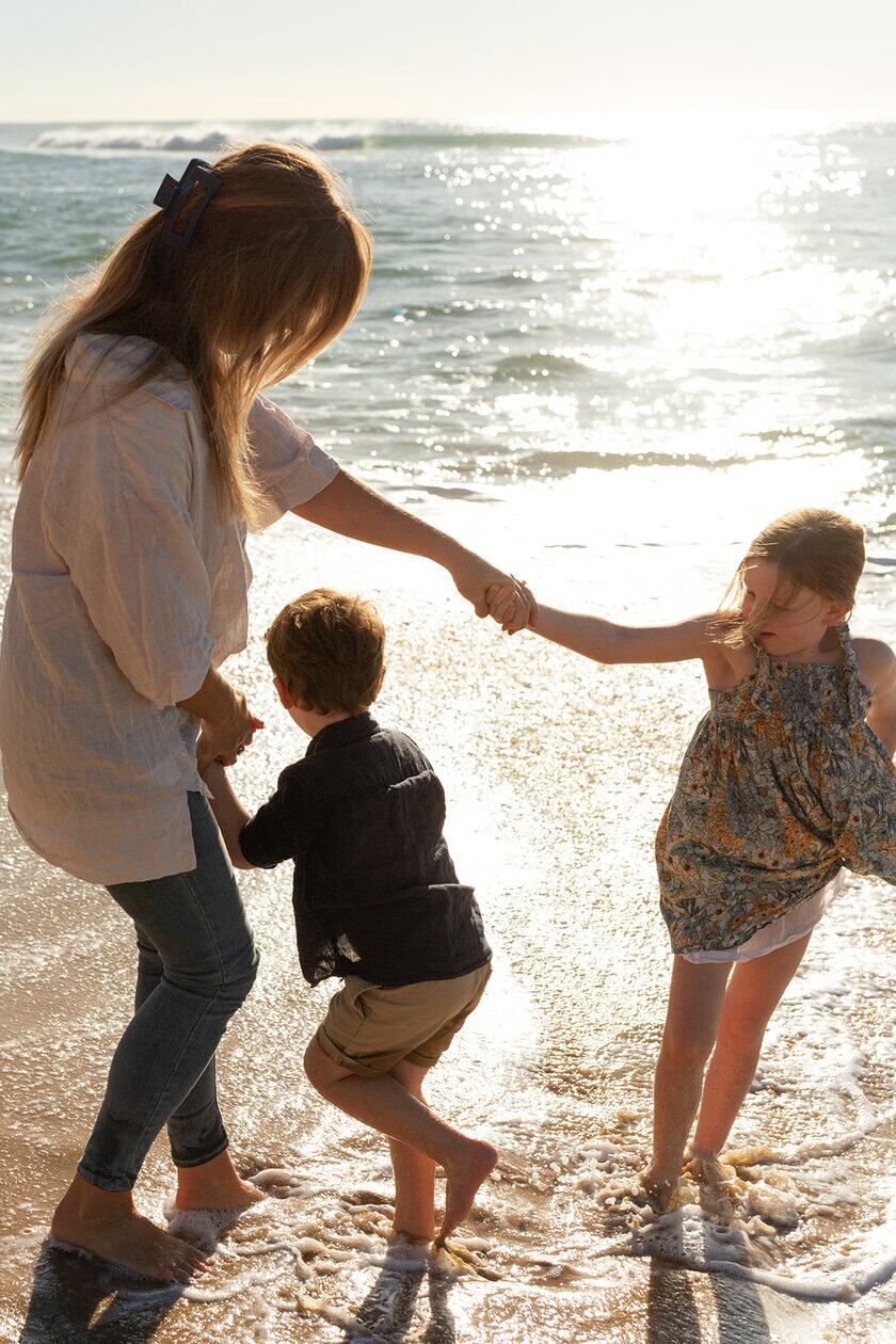 A parent holding hands with two children at the water’s edge