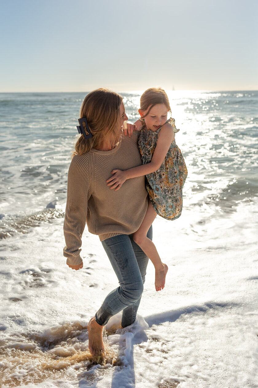 A parent carrying their child through shallow water at the beach