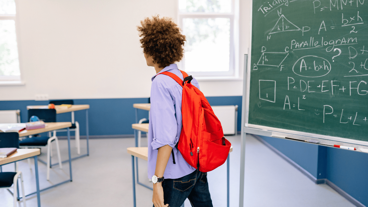 student with red backpack walking through classroom