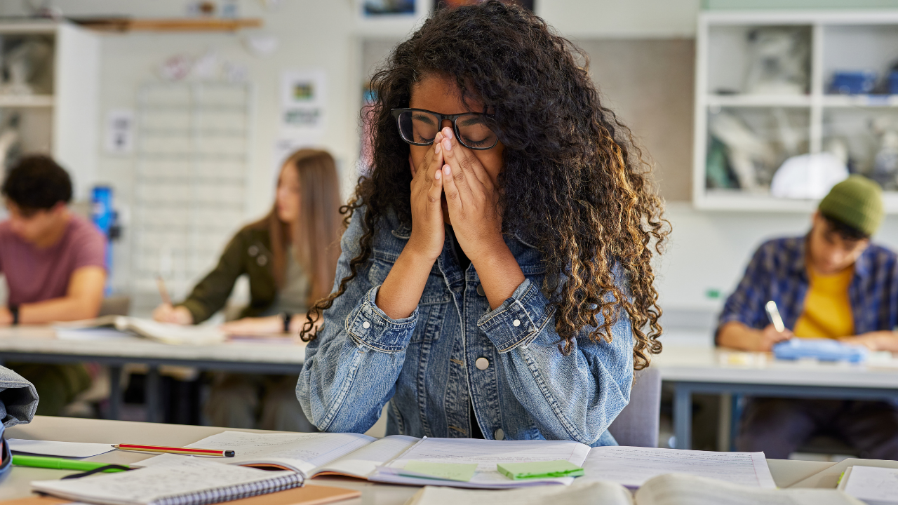 student with face in hands at desk in classroom