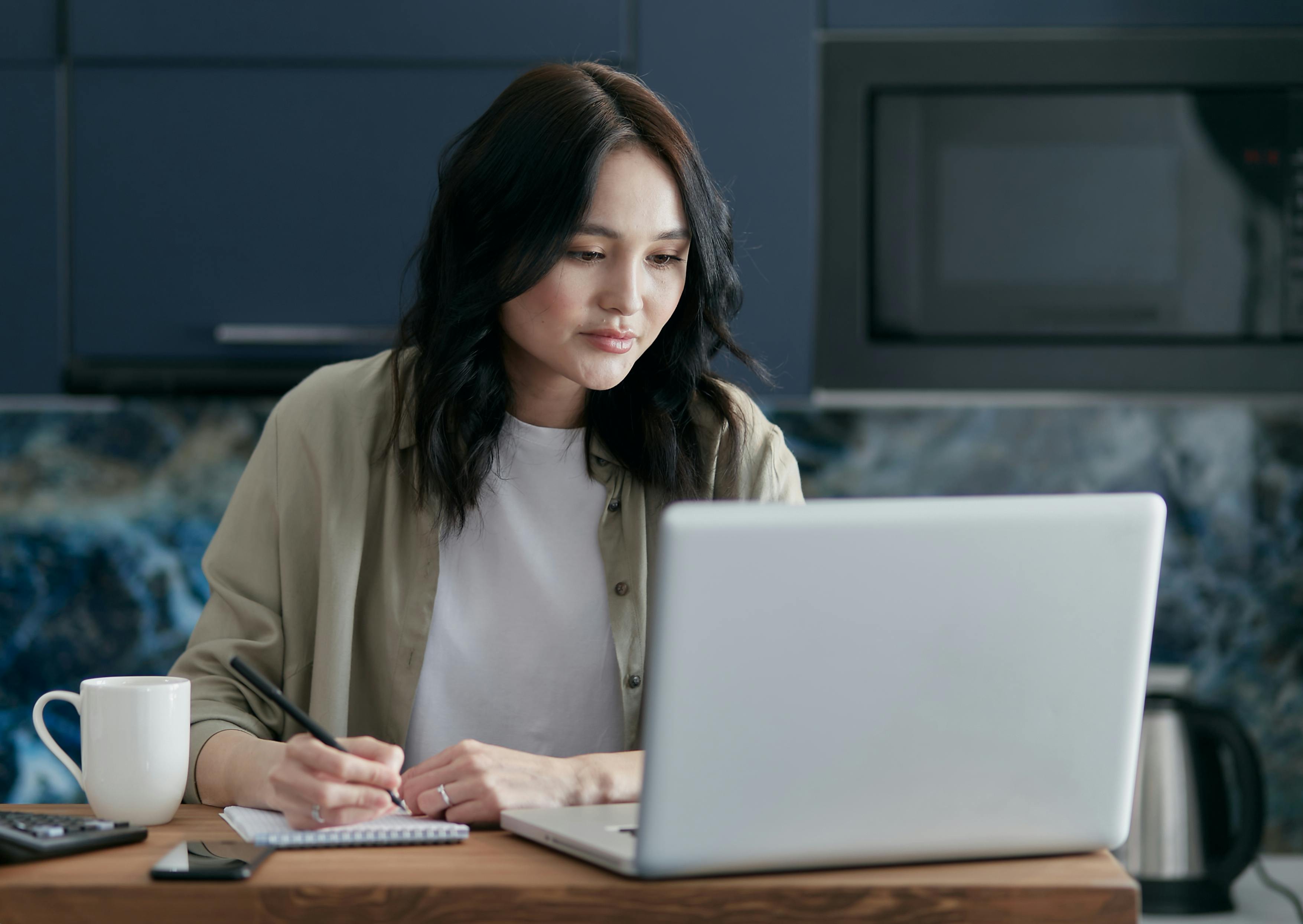professional reviewing certification materials on laptop at clean modern desk with notebook and coffee