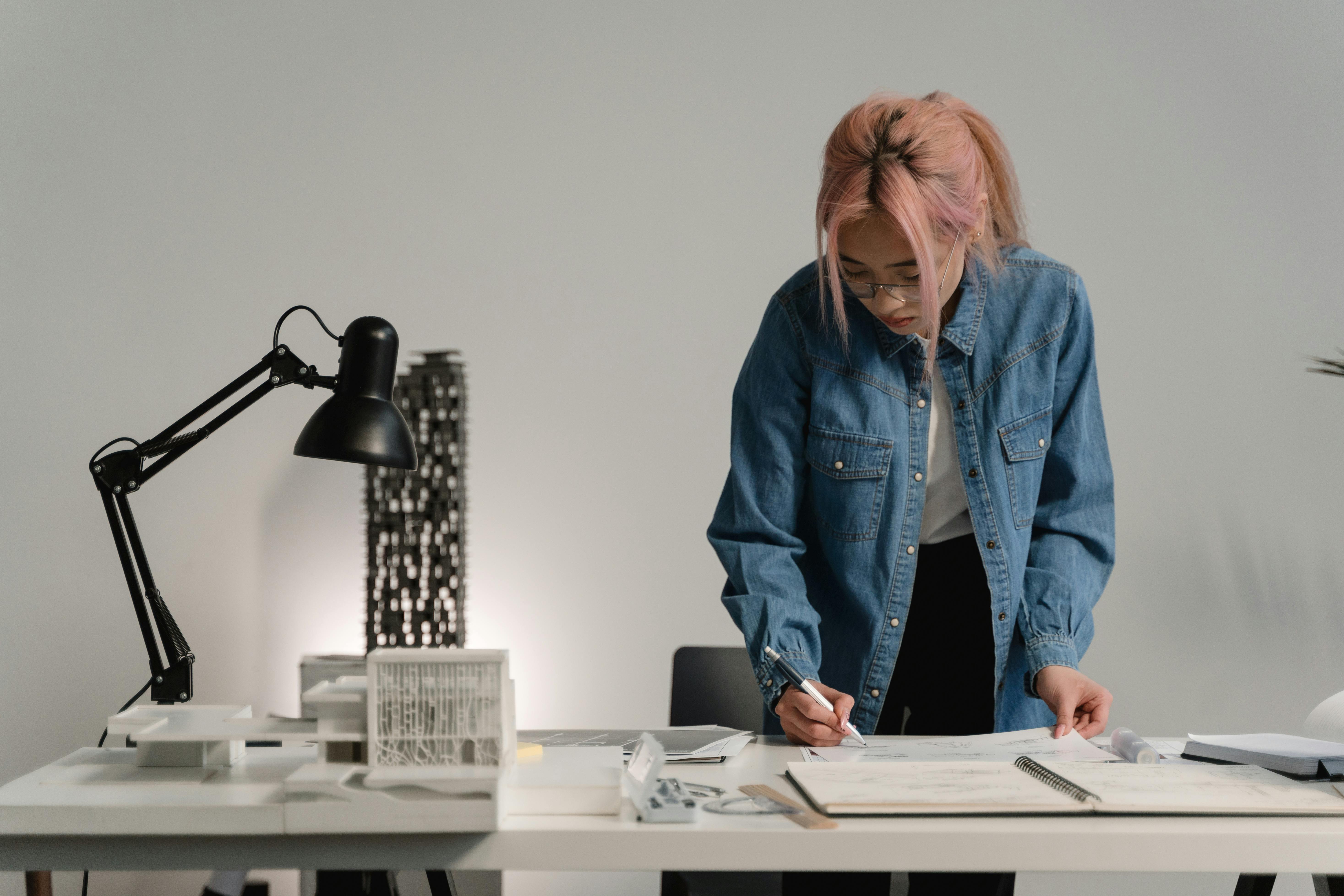 young professional reviewing creative project plans at a desk with sketches and a laptop in a bright modern studio