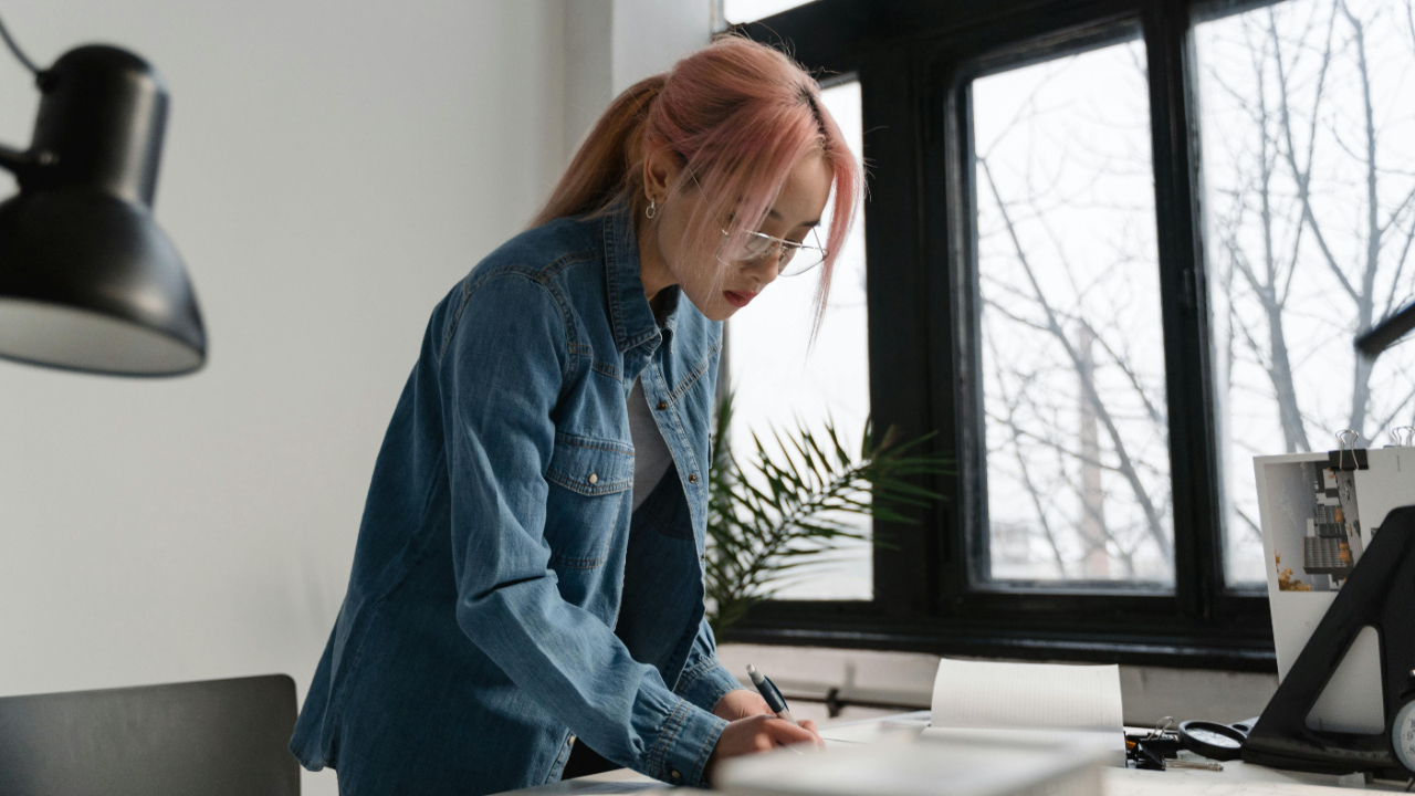 Designer transitioning to project management role at desk with both sketches and project planning documents in a bright modern studio office