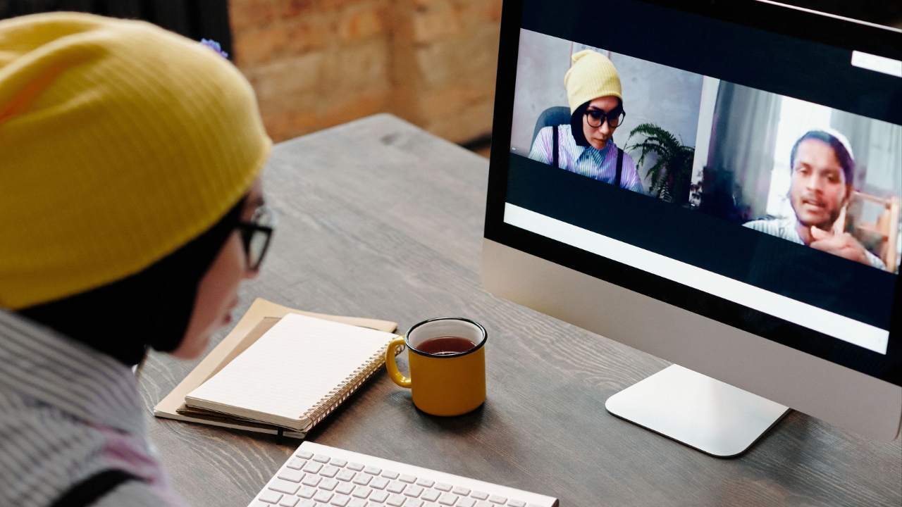 Creative project manager coordinating with a freelance designer over a video call with project notes and a laptop on a modern office desk
