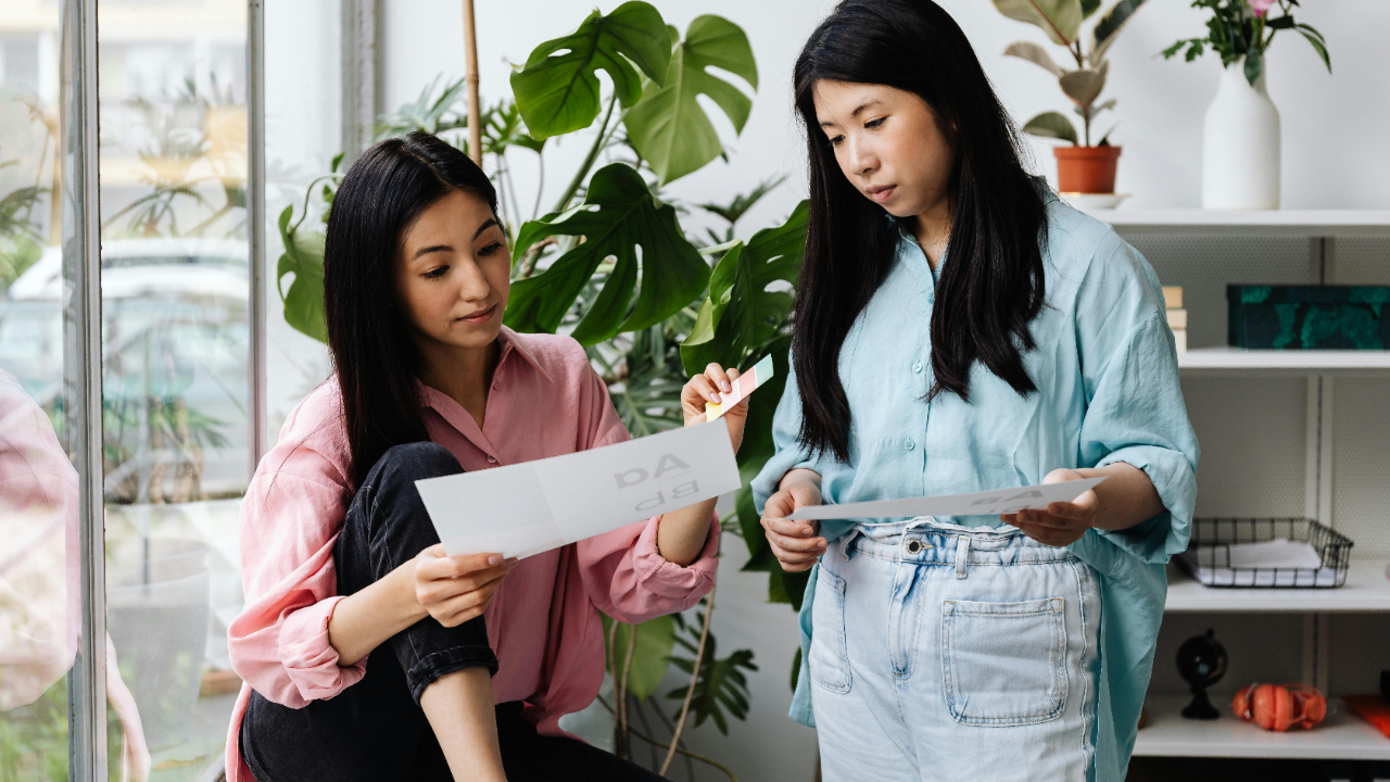 Professional women reviewing certification documents at a desk in a modern creative studio office