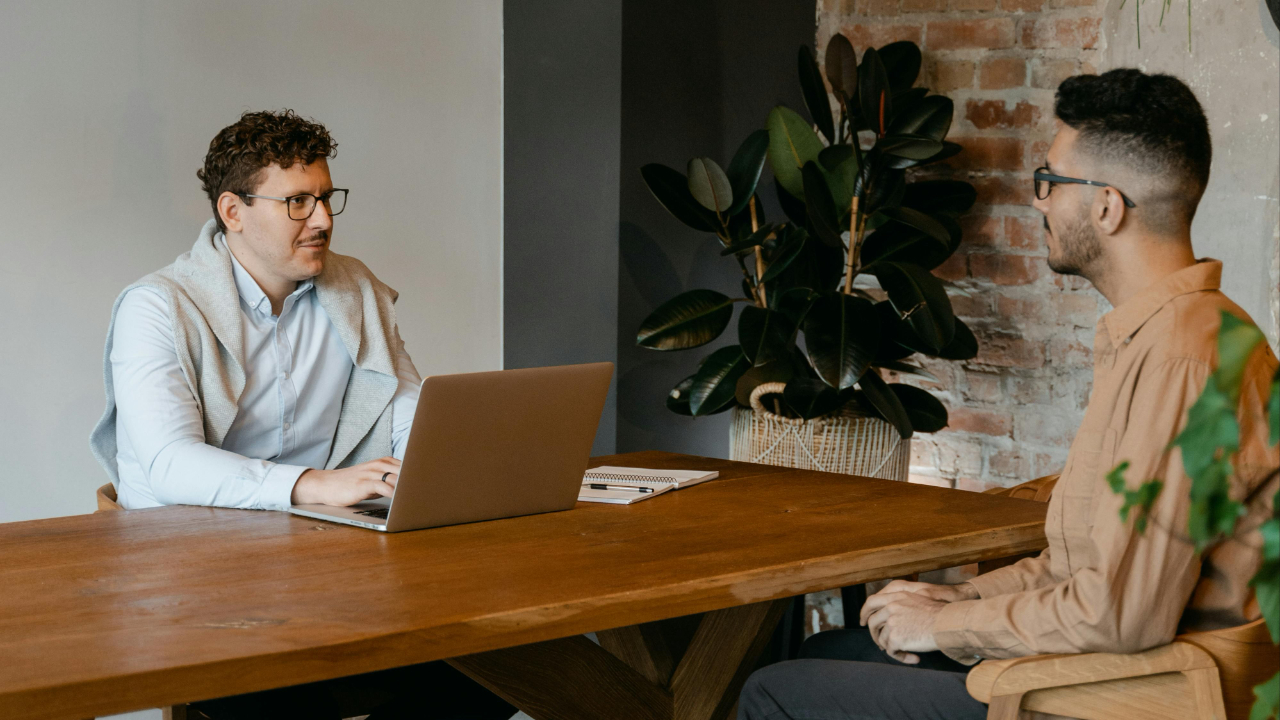 Professional candidate sitting across from a hiring manager in a bright modern conference room during a job interview with notebook and laptop on the table