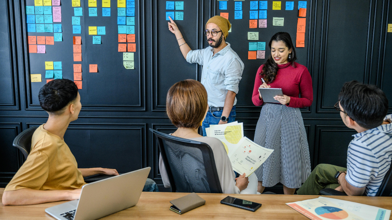 Creative project manager walking team through phased project plan on whiteboard with sticky notes in a bright modern agency conference room
