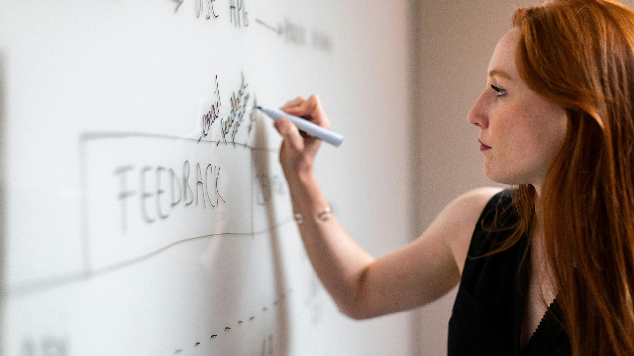 Creative project manager mapping a project timeline with sticky notes and a calendar on a whiteboard in a bright modern agency office