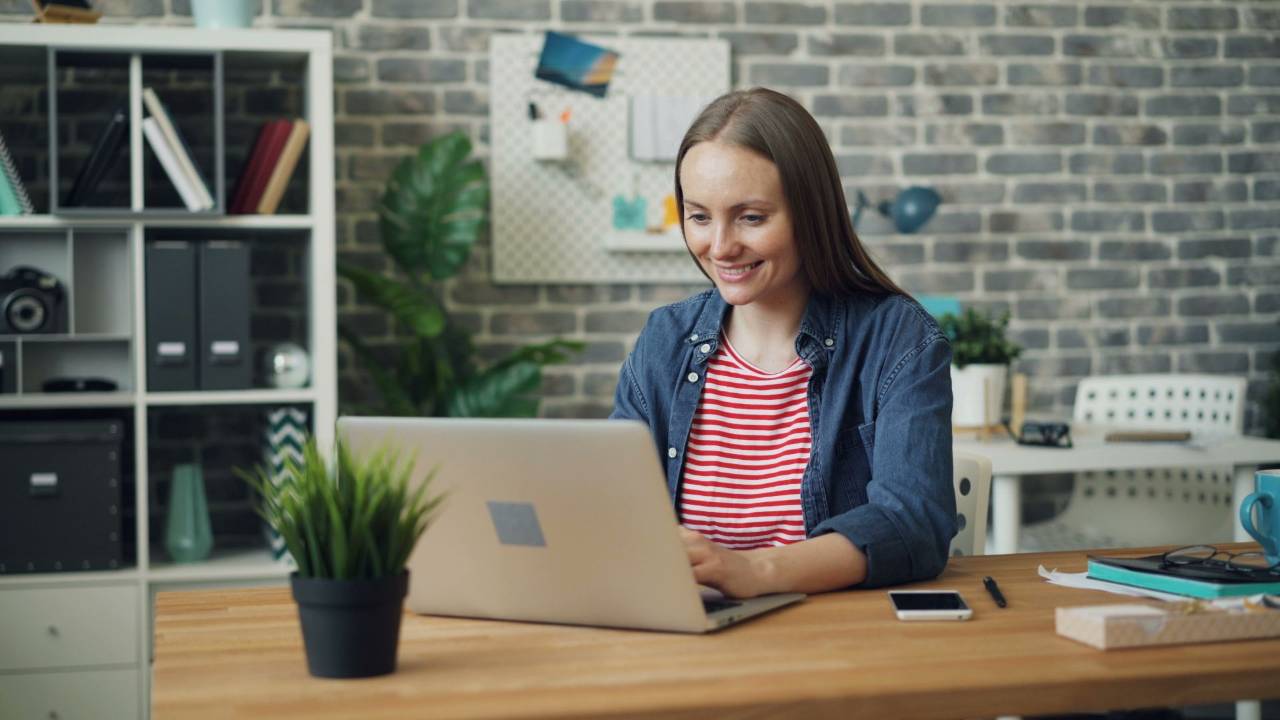 Creative project manager typing a reply on a laptop at her desk in a bright office.
