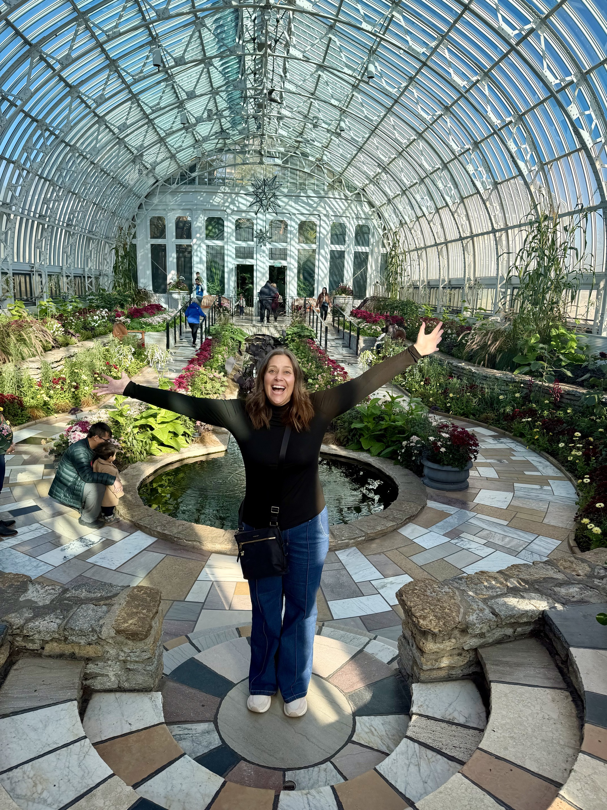 Kara with her arms wide open in a glass conservatory