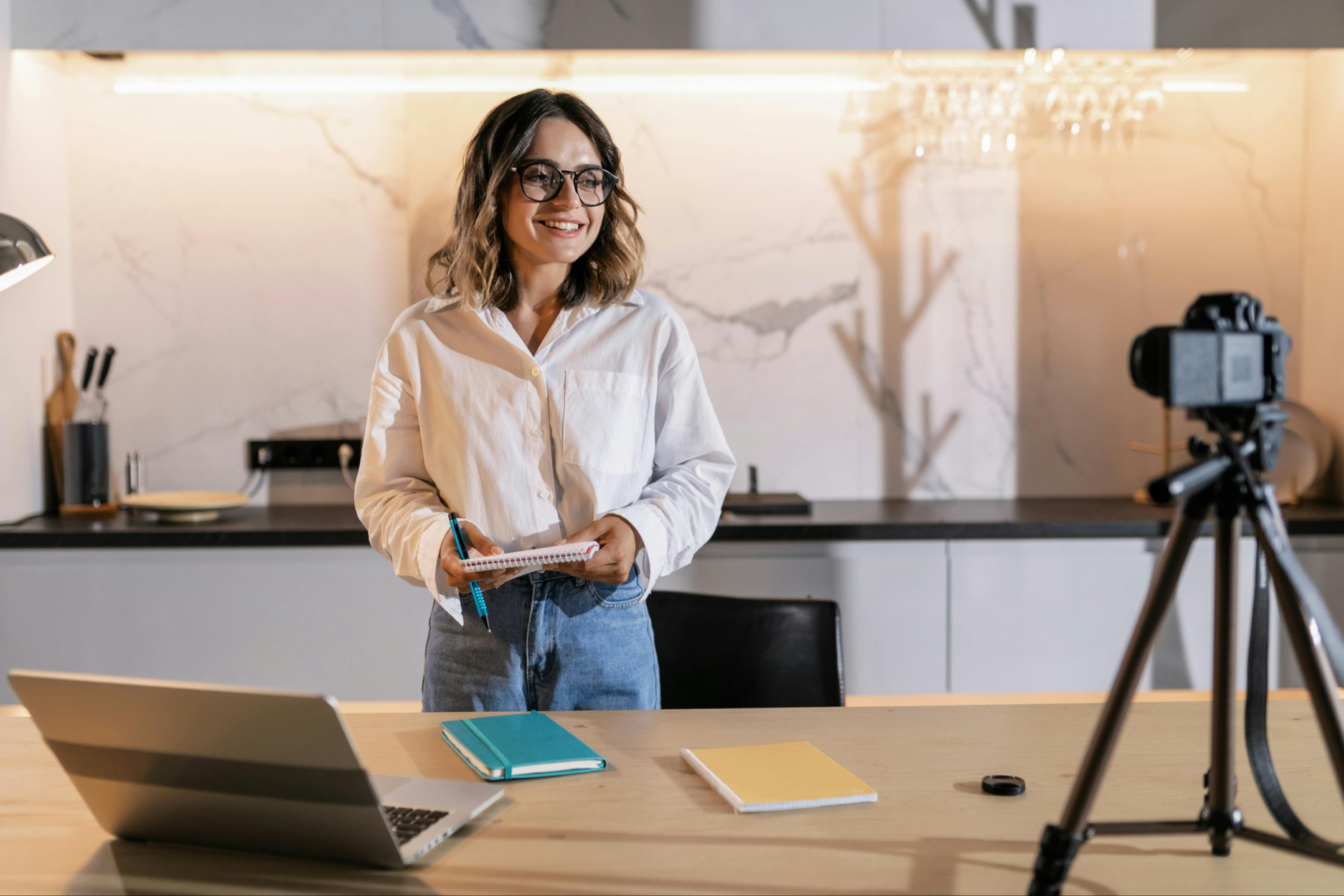 Confident young woman smiling with a laptop, notebook, and pen on the table — ready to take action and move forward with her goals.
