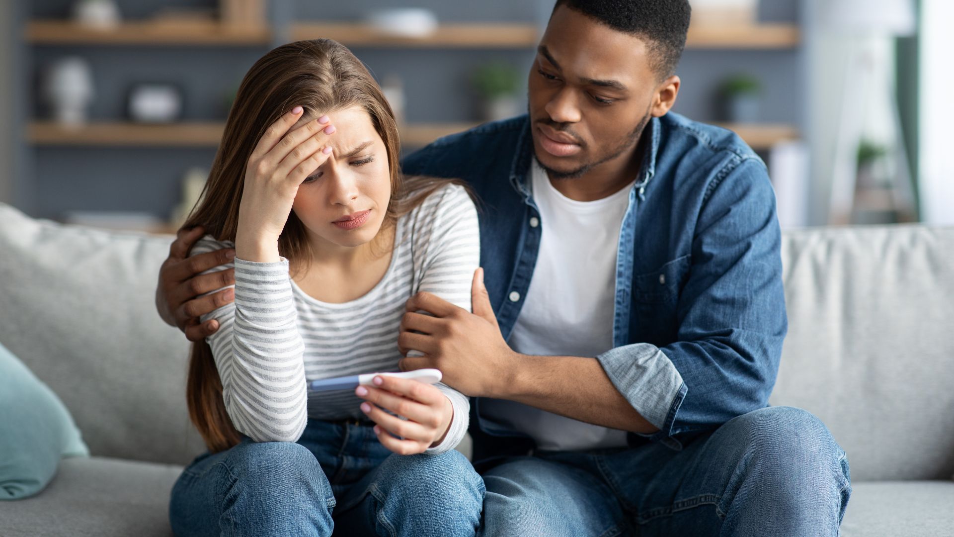 A woman looking at a pregnancy test while her partner comforts her