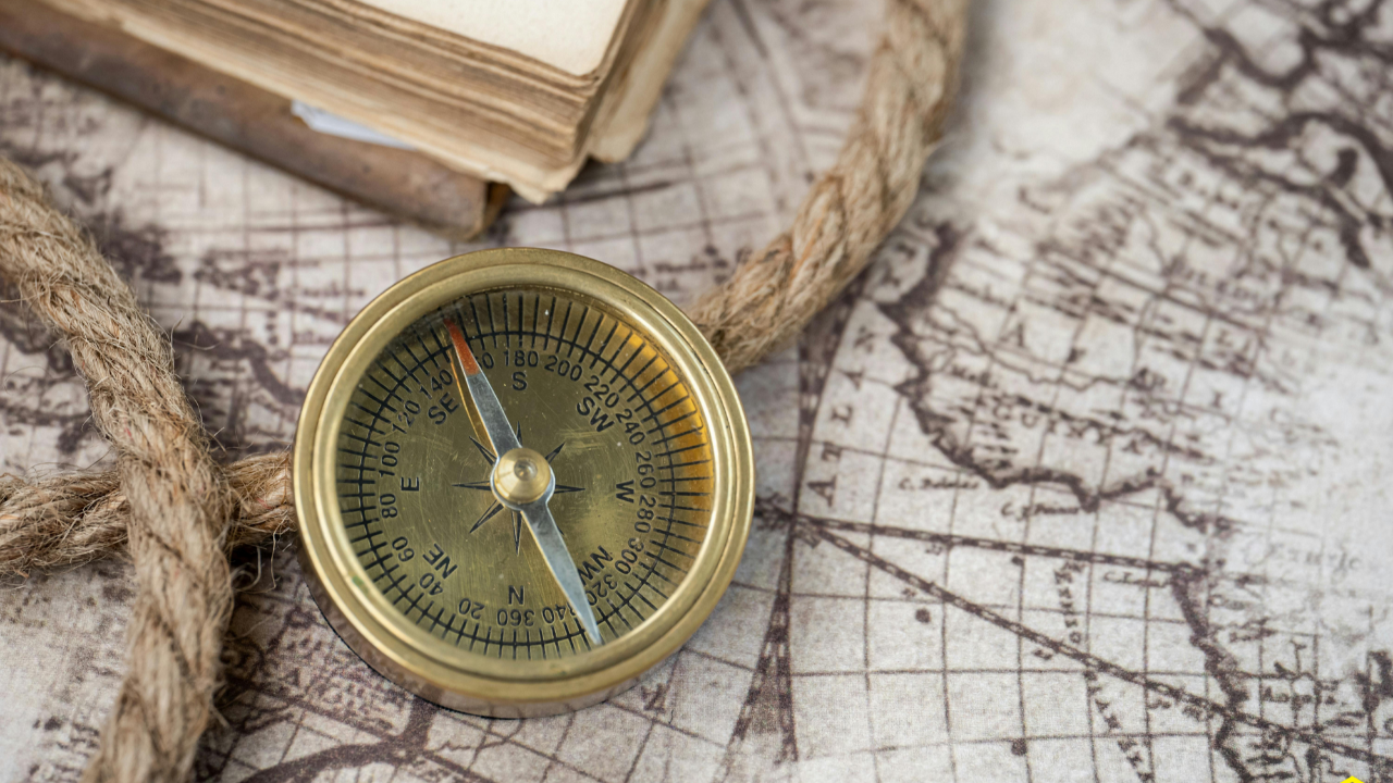 A brass compass resting on a map beside a journal and rope, symbolizing the difference between having information and having orientation. The image represents finding your bearings, understanding your position, and navigating life's complexity with greater clarity and purpose through Cube Philosophy.
