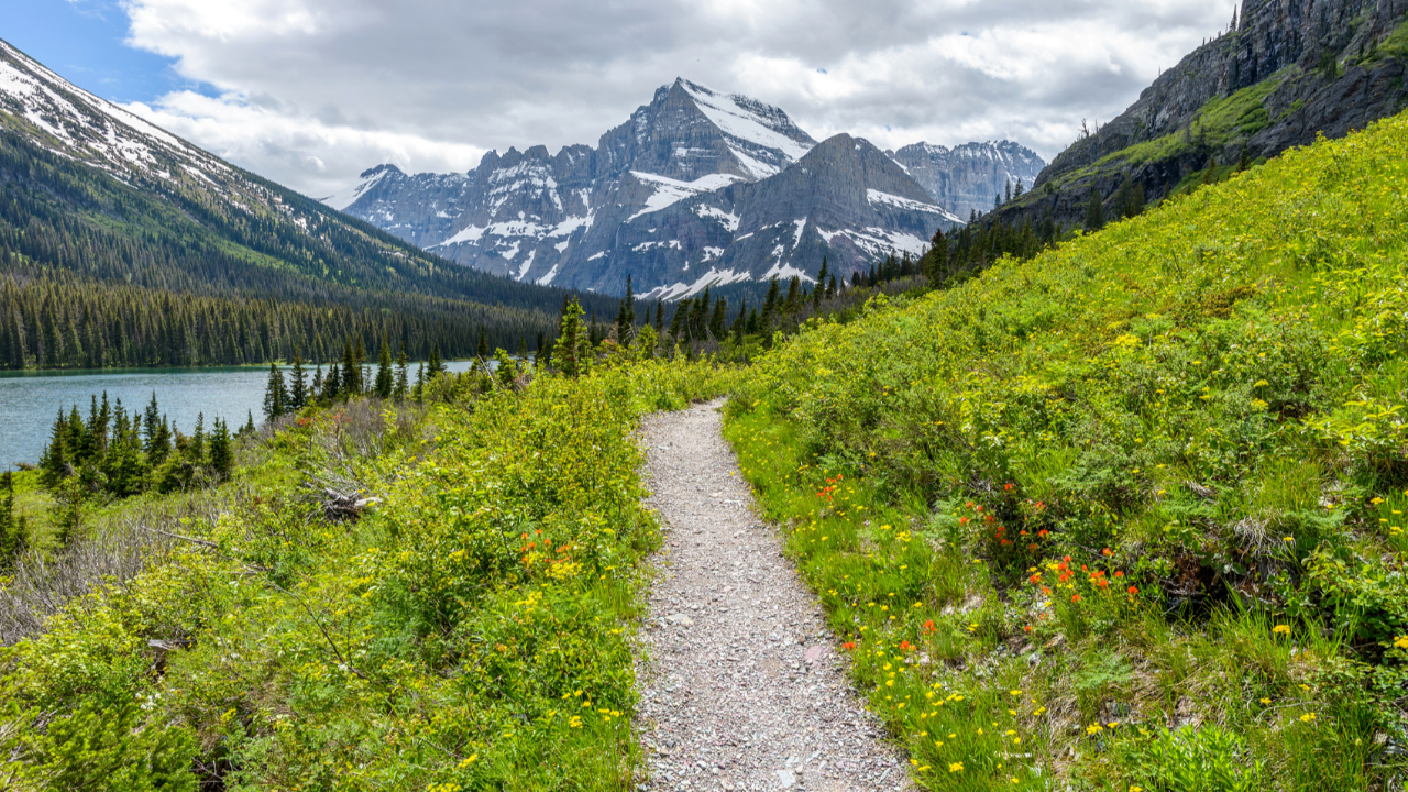 Mountain trail beside a lake leading toward snow-covered peaks, representing Compass · Journey · Home and the movement from direction to development and return in Jacob Goettsche's my K.I.N./G-M.A.P.