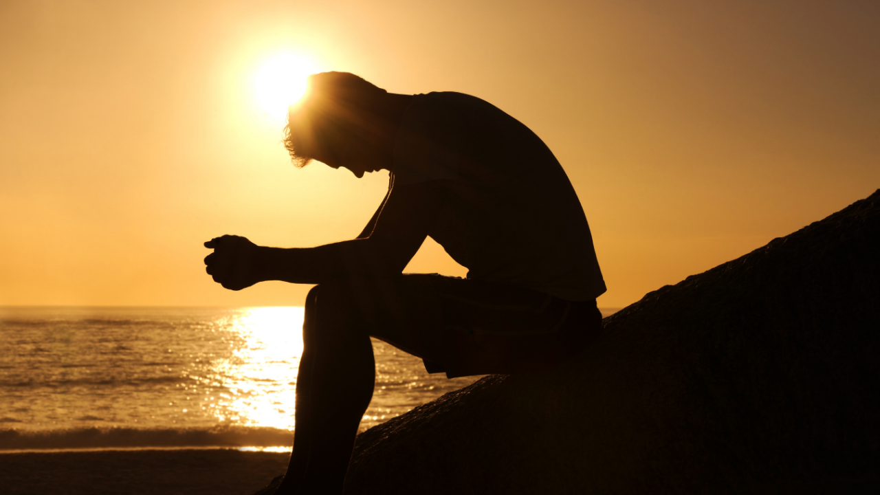 Silhouette of a seated man leaning forward beside the ocean at sunset, representing physical awareness and the body recognizing change before the conscious mind.