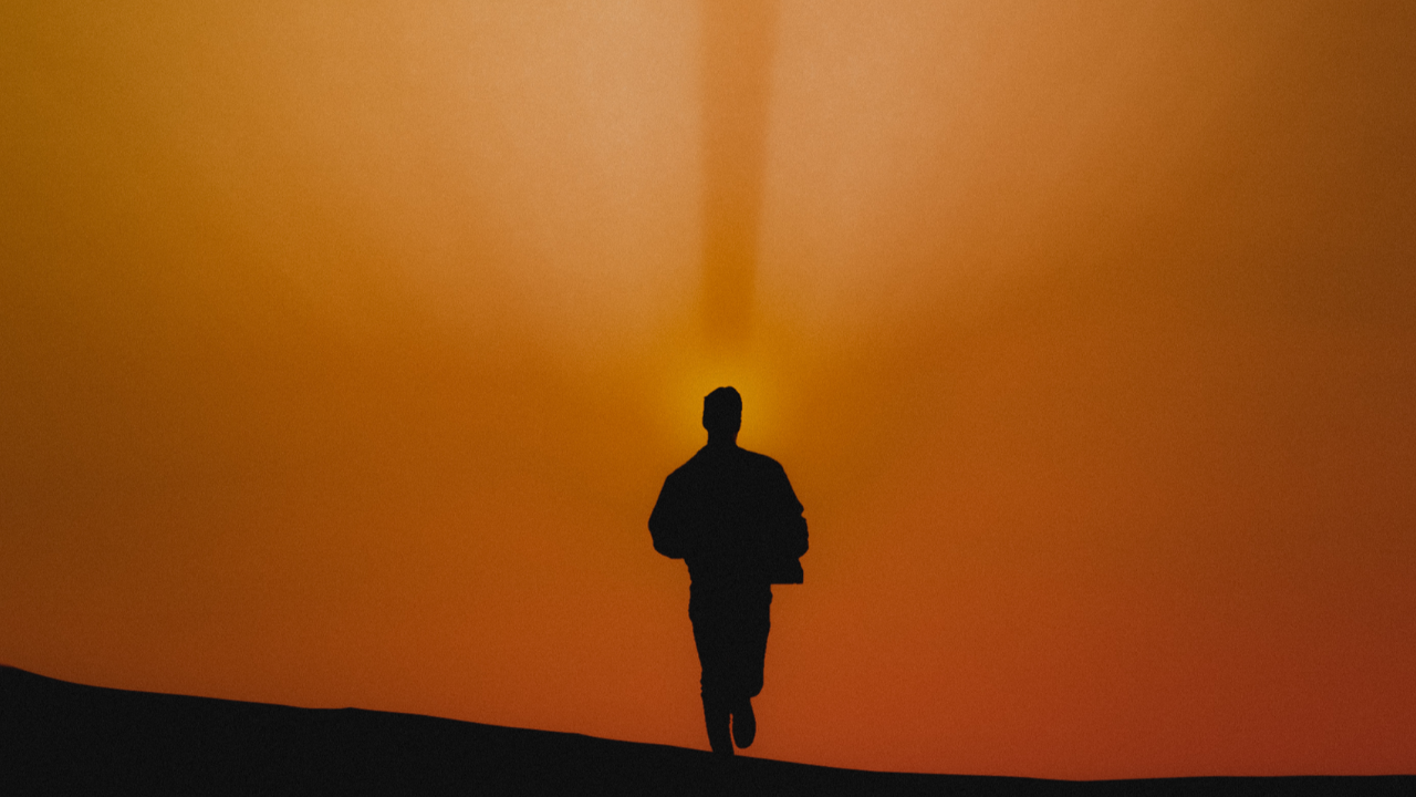 Silhouette of a person moving across a ridge beneath an orange sky, representing stability, Ground, orientation, and conscious movement in Cube Philosophy.