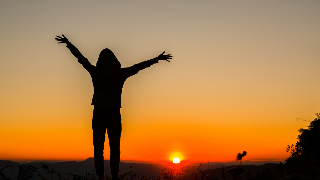 Silhouette of a person standing with arms open beneath a glowing sunset, representing Breathe, Observe, Orient, Return, Compassion, and Discern in Living Cube Philosophy.
