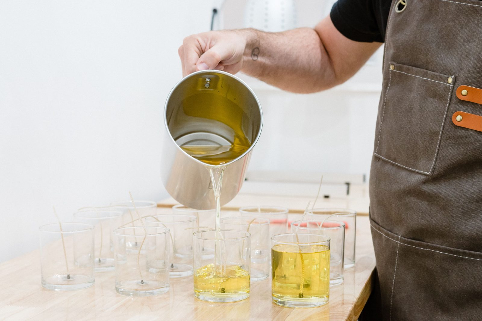 Pouring melted wax from a steel pitcher into glass candle jars