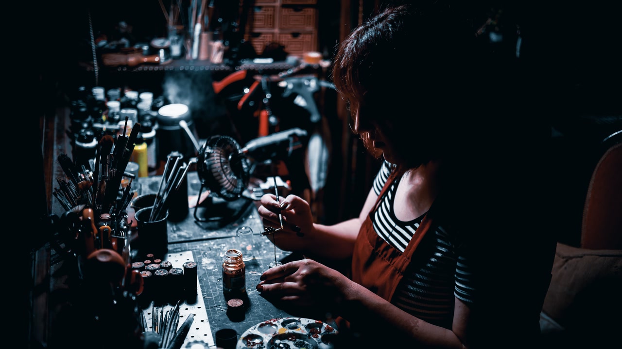 Artista pintando una miniatura con un pincel en un taller oscuro.