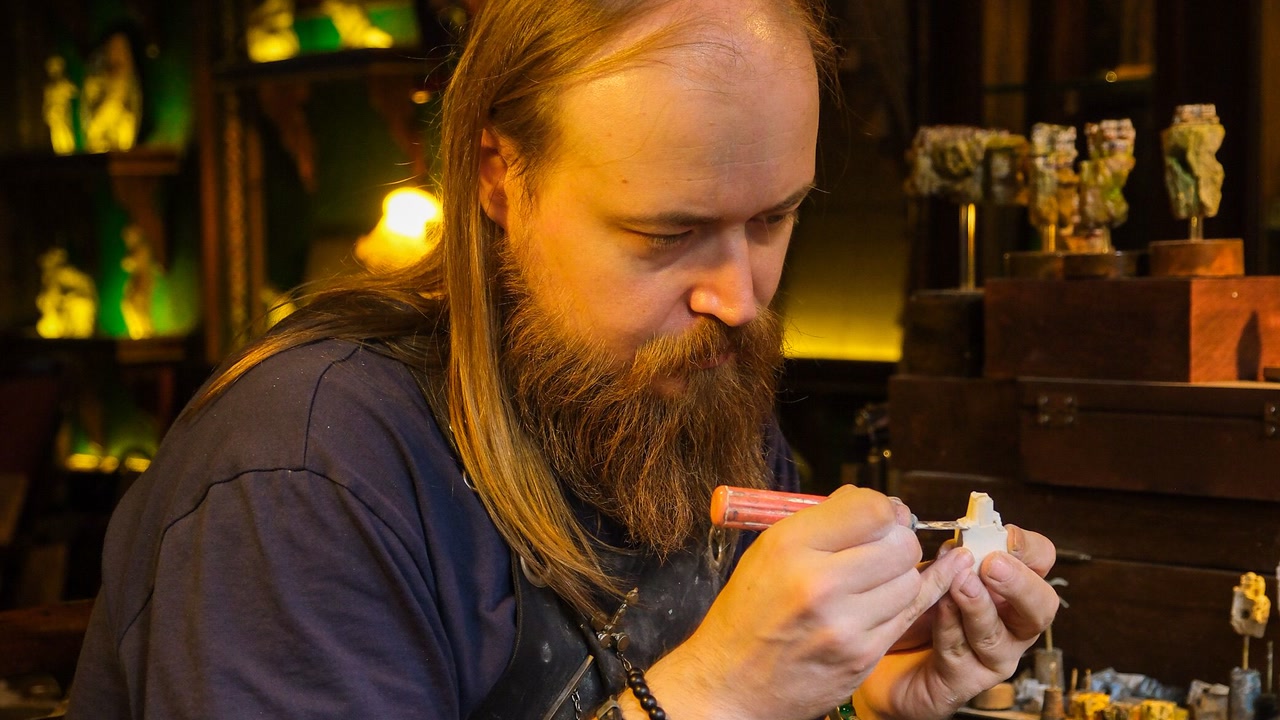 Artesano pintando una pequeña figura con pincel en un taller.