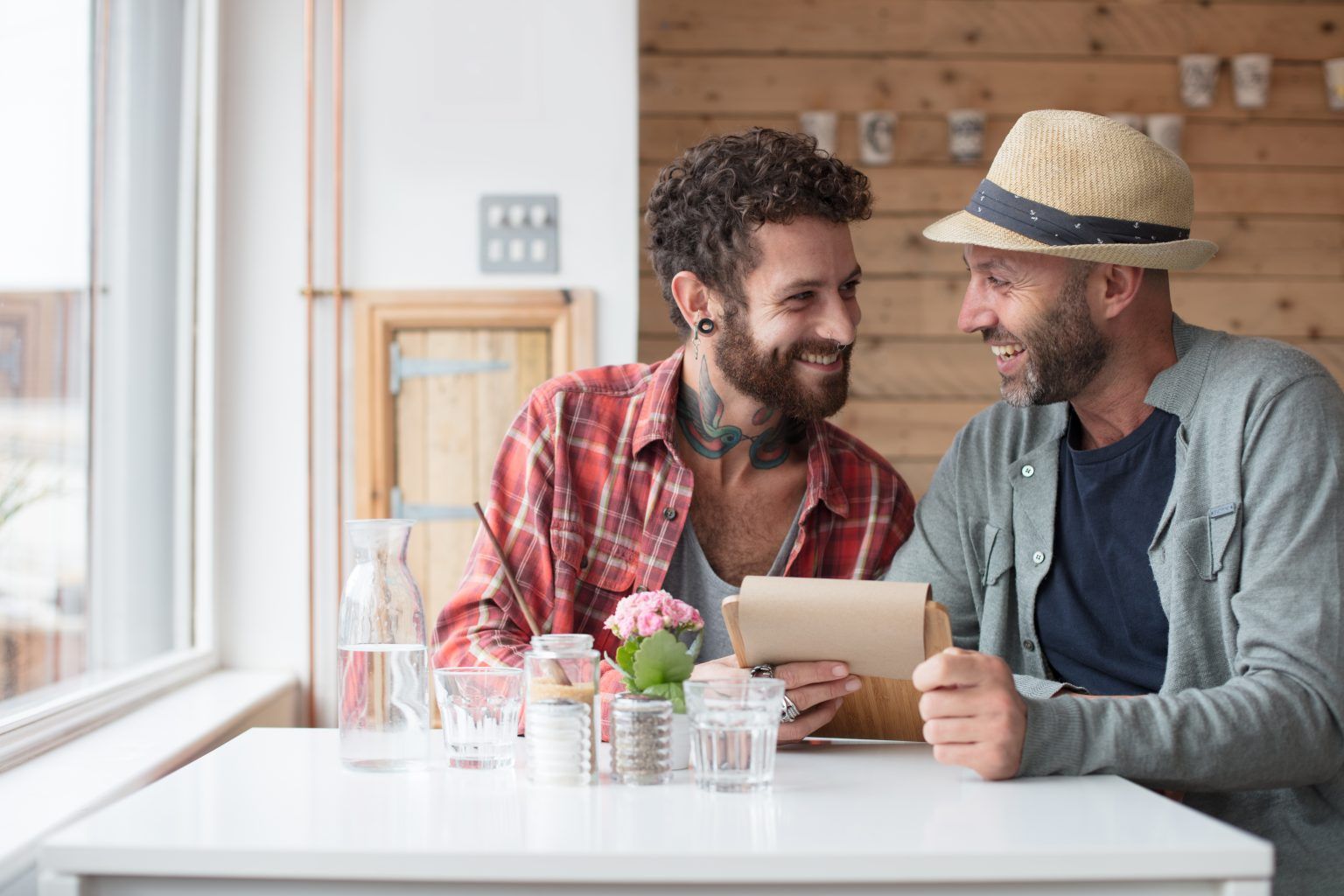 Stylish gay couple laughs together in cafe
