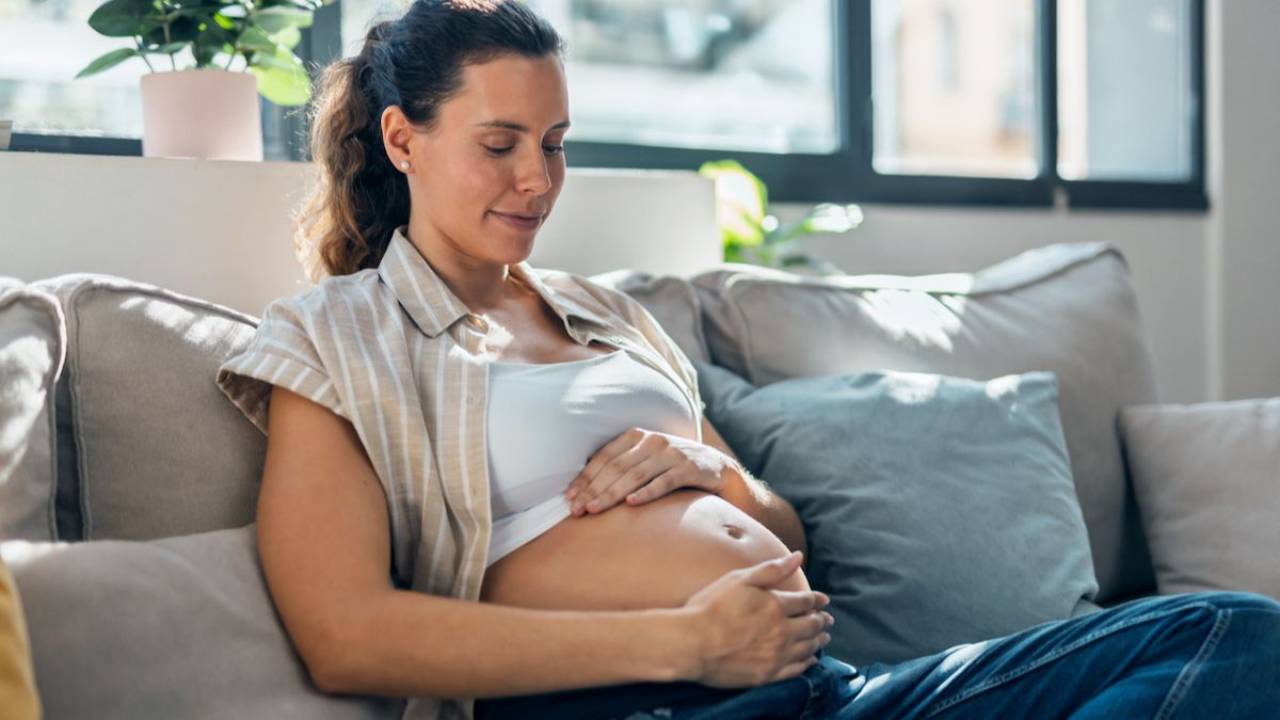 pregnant woman sitting on couch with hands around her belly