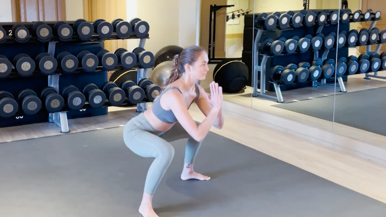woman in grey leggings and sports bra in a gym performing a squat