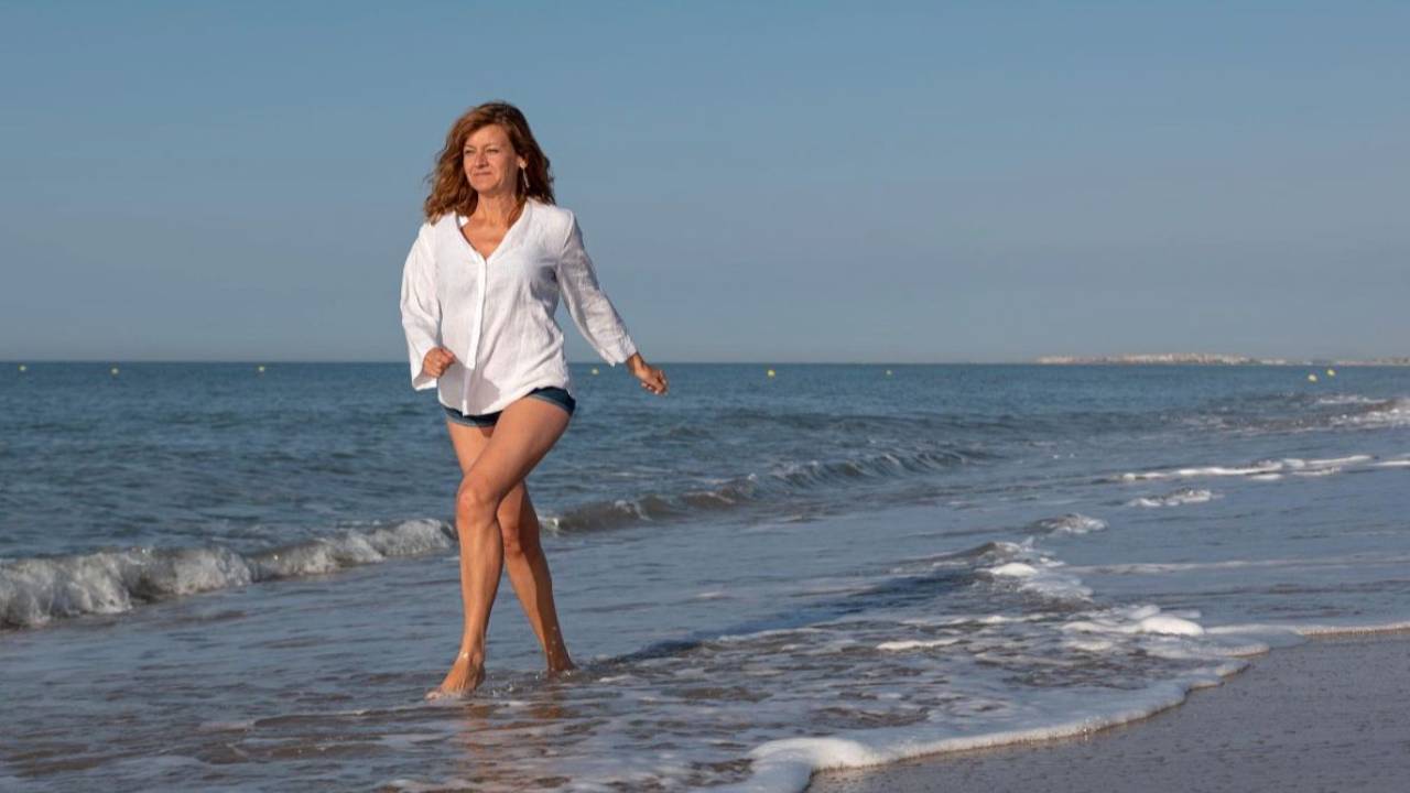 woman in white shirt and jean shorts walking on beach